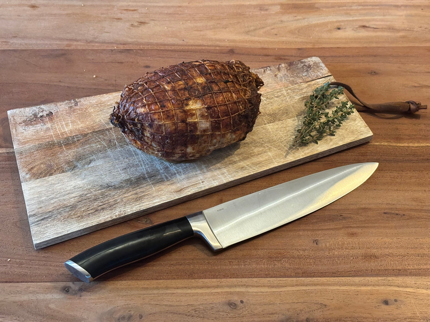Gebraden kiprollade op een houten plankje. Naast het plankje ligt een koksmes. Op de hoek van het plankje ligt een takje tijm.