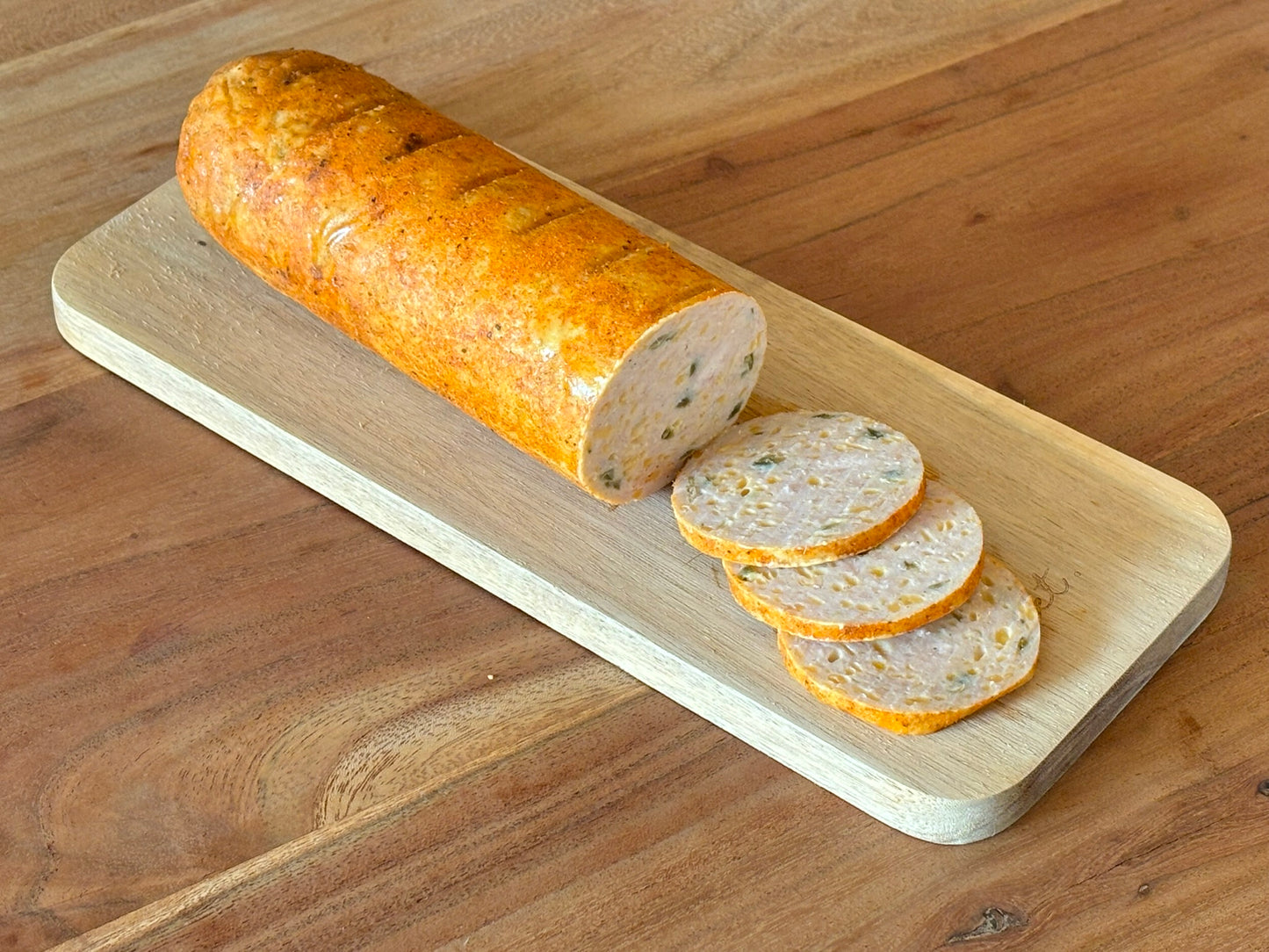 Een kip grillworst, deels in plakken gesneden, ligt op een rustieke houten plank. De grillworst heeft een gekruide buitenkant en ziet er sappig uit, met duidelijk zichtbare, malse plakken kippenvlees.