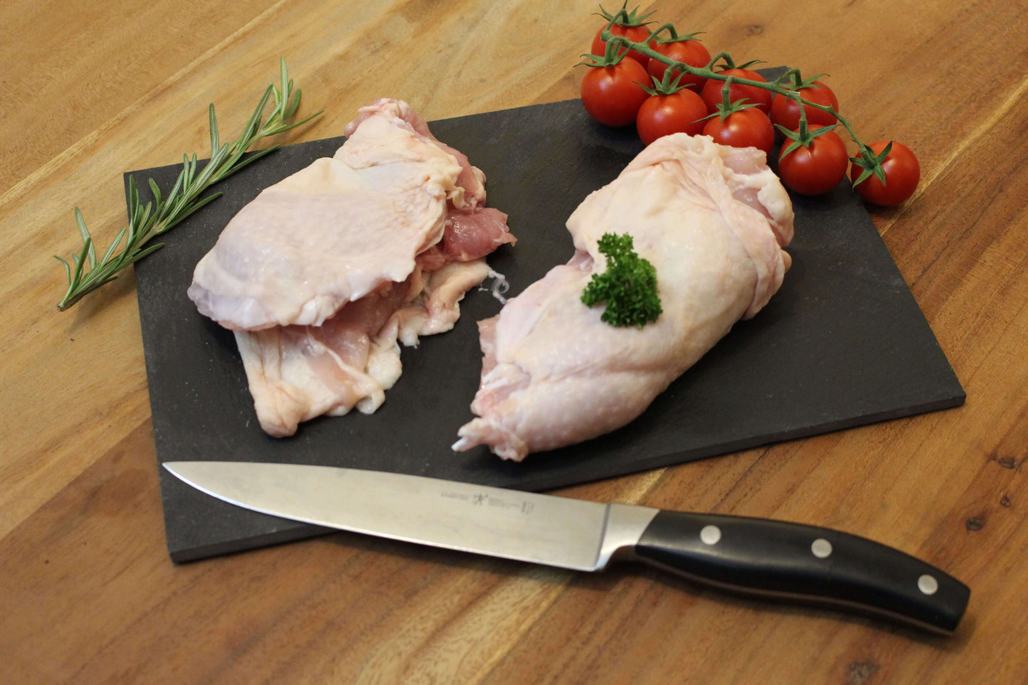 Twee pootvlees op een zwart plankje. bij de het plankje ligt een garnering van peterselie, cherrytomaten en naast het pootvlees ligt een takje tijm. naast het plankje ligt een koksmes.