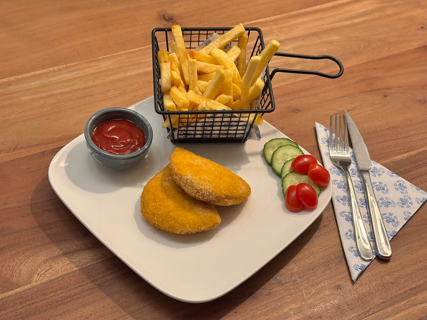 Gebakken kip cordon bleu XL met een knapperige korst, gevuld met smeltende kaas en ham. Geserveerd met krokante aardappelpartjes en een frisse salade op een houten eettafel.