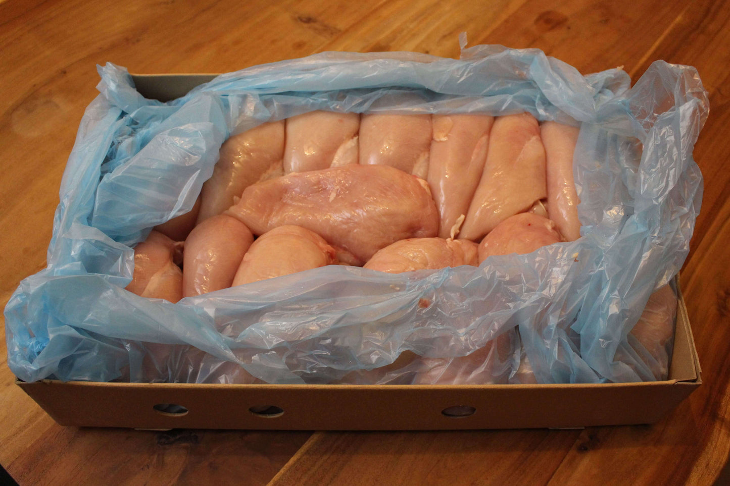 deze bulkverpakking is een kartonnen doos met daarin een blauwe plastic zak gevuld met verse, sappige kipfilet. de doos staat op een houten tafel.