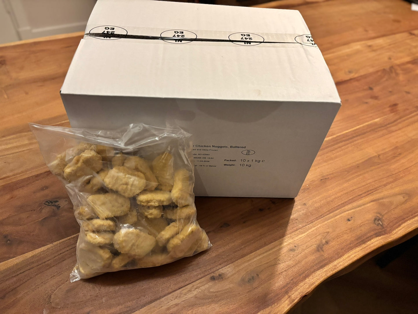 Een witte doos en een zak gevuld met goudbruine kip nuggets. de verpakking staat op een houten tafel.