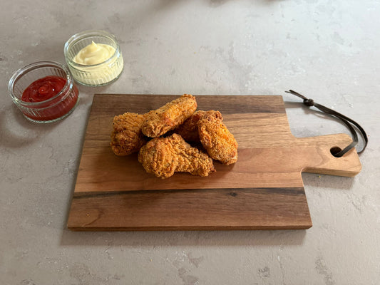 Krokante kip hotwings geserveerd op een houten borrelplank op een leisteen ondergrond. Ze hebben een krokante paneer laag .Het product is geserveerd met een glazen schaaltje ketchup en mayonaise.