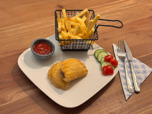 Gebakken kip saté schnitzel met een knapperige korst, gevuld met satésaus. Geserveerd met krokante aardappelpartjes en een frisse salade op een houten eettafel.