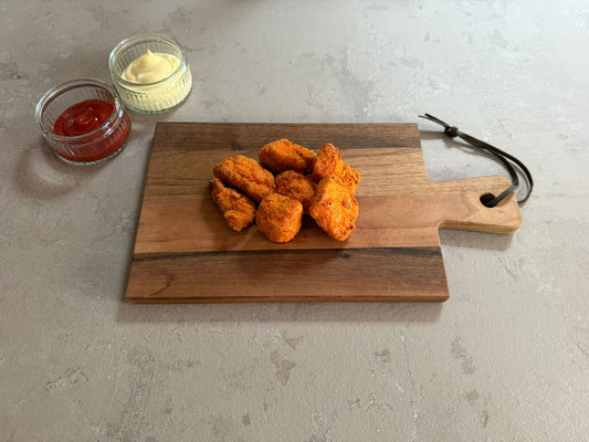 Krokante kip hot chili chunks geserveerd op een houten borrelplank op een leisteen ondergrond. Ze hebben een krokante paneer laag .Het product is geserveerd met een glazen schaaltje ketchup en mayonaise.