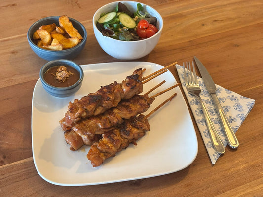 Gebakken kipsaté met een knapperige korst, gemarineerd met een café de paris marinade. Geserveerd met krokante aardappelpartjes en een frisse salade op een houten eettafel.