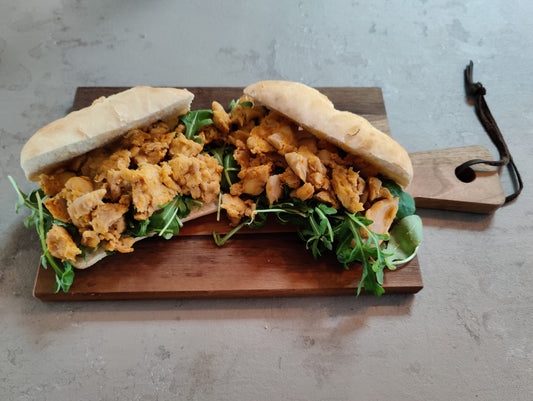 Twee broodjes gevuld met malse, sappige kipdijblokjes met licht pikante piri piri marinade op een bedje van coleslaw en rucola. geserveerd op een rustiek houte plankje op een grijs aanrechtblad