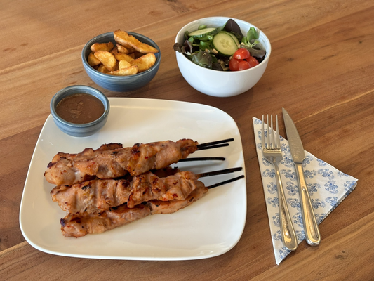 Gebakken kipsaté piri piri met een knapperige korst, gemarineerd met een piri piri marinade. Geserveerd met krokante aardappelpartjes en een frisse salade op een houten eettafel.