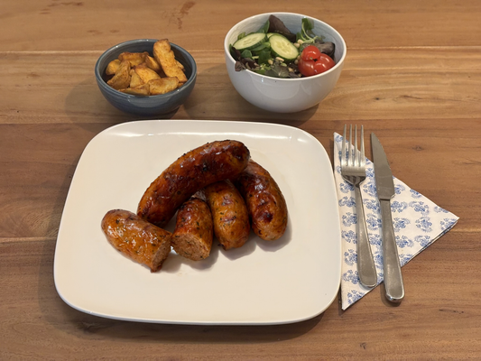 Gebakken kipworsten met een knapperige korst, gevuld met een jalepeno cheddar vulling. Geserveerd met krokante aardappelpartjes en een frisse salade op een houten eettafel.