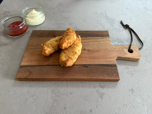 Krokante kiphaasjes geserveerd op een houten borrelplank op een leisteen ondergrond. Ze hebben een krokante paneer laag. Het product is geserveerd met een glazen schaaltje ketchup en mayonaise.