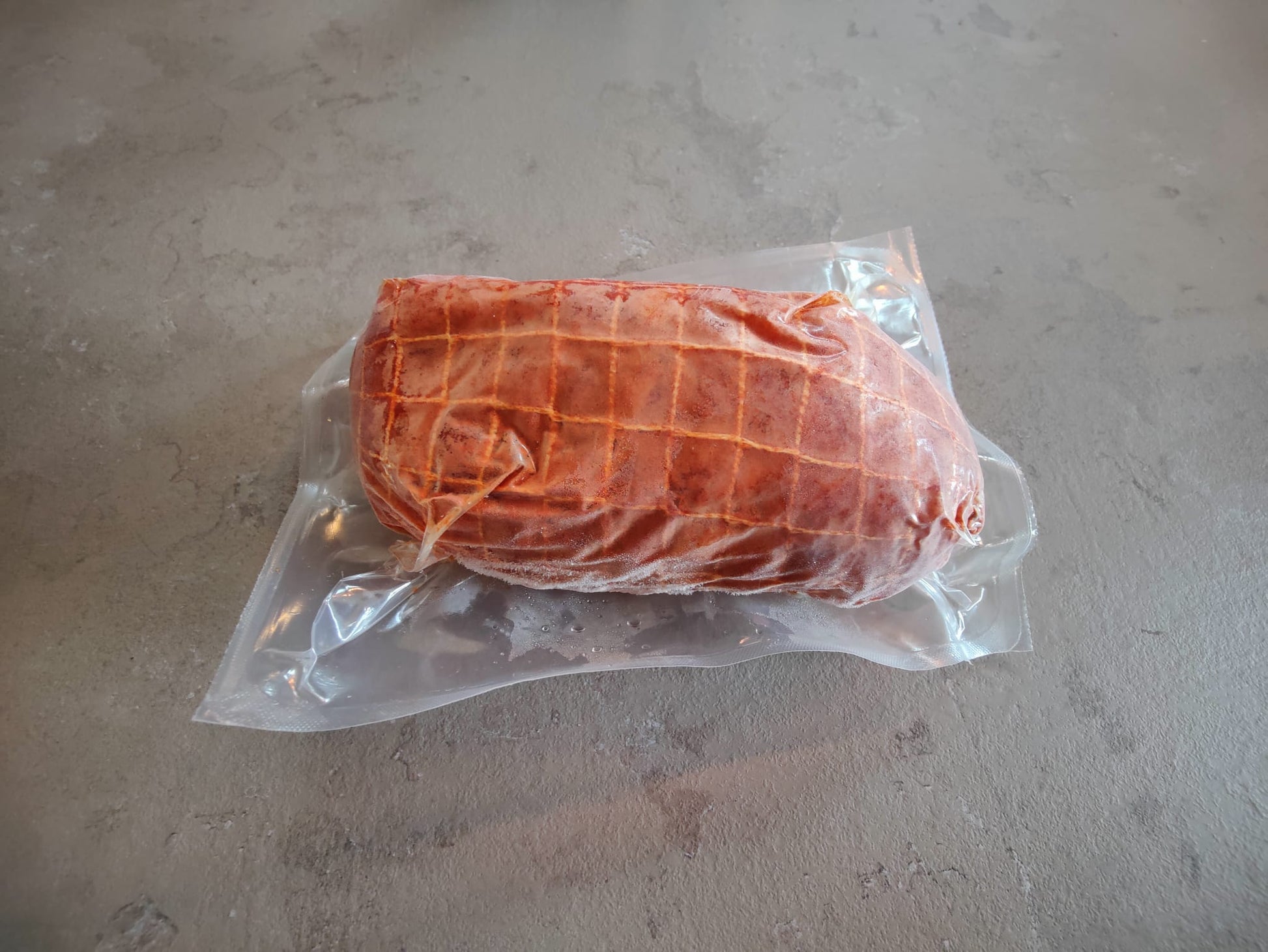Een diepgevroren rip rollade in een plastic vacuümverpakking op een grijze stenen blad. 